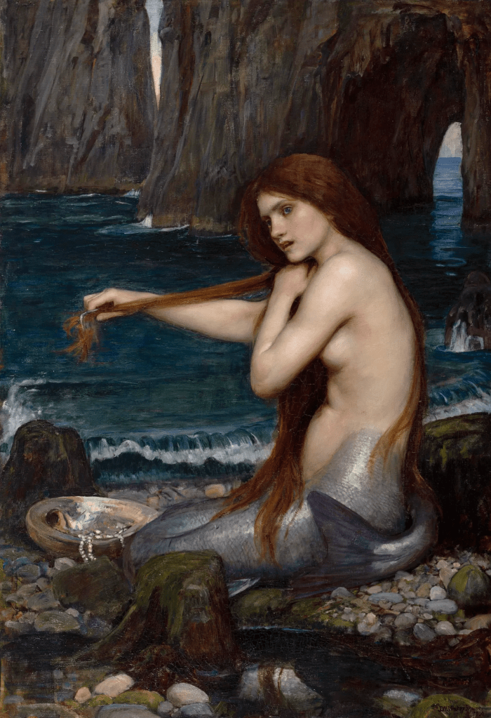 A solitary mermaid sits on coastal rocks at the water’s edge, combing her long hair beside dark blue sea water; an open shell with pearls rests near her feet, with steep sea cliffs behind.