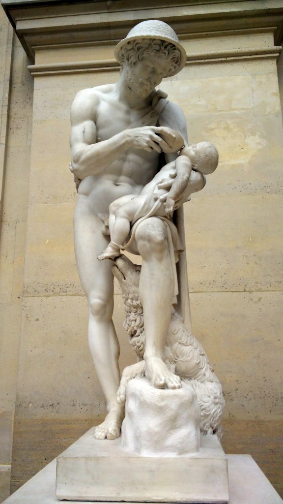 A white marble neoclassical sculpture depicting the shepherd Phorbas holding the infant Oedipus in his arms. The barefoot shepherd gazes downward at the child with concern and tenderness, while a dog at his feet gently licks the infant’s exposed foot. The baby’s small body rests across the shepherd’s forearm, emphasizing vulnerability, rescue, pity, and the fragile mercy that preserved Oedipus’s life.